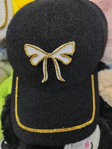 Detail of knitted baseball cap featuring rhinestone bow ornament and studded brim edge
