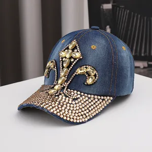 Detailed close-up of a blue denim baseball cap featuring an ornate rhinestone fleur-de-lis