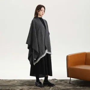 Close-up of dark grey knit poncho featuring thick fabric and white tassel fringe detailing
