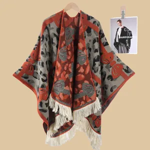 Nahaufnahme des Strickponchos mit orange-schwarzem Leopardenmuster und weißen Quasten
