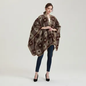 Detail eines Winter-Strickponchos mit braunem Karomuster und Herzmotiv-Stickerei