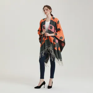 Detail of knitted poncho featuring orange and grey color blocks with pink polka dots and tassels