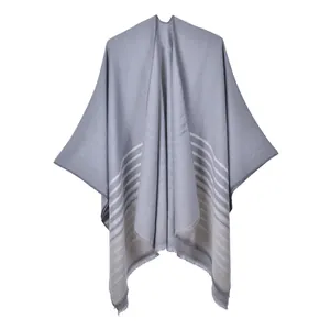 Détail d'un poncho en maille grise avec rayures blanches et finitions à franges