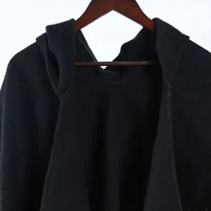 Detail of a black hooded poncho with thick fabric texture on a wooden hanger