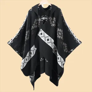 Detail of hooded black knitted poncho with gray geometric patterns and bohemian tassels