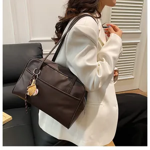 Detail view of coffee brown tote bag with baseball charm on a soft leather couch