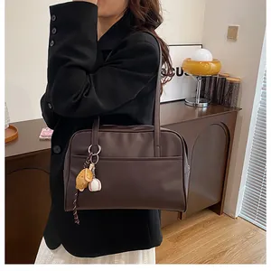 Detail of dark brown leather tote bag with miniature baseball glove charm and zipper closure