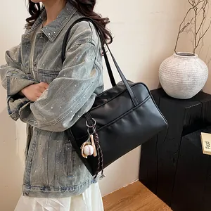 Large black leather tote bag with baseball charm shown on shoulder by female model