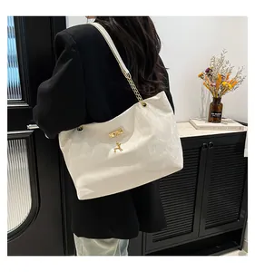 Detail of a creamy white tote bag featuring a gold deer charm and chain shoulder strap