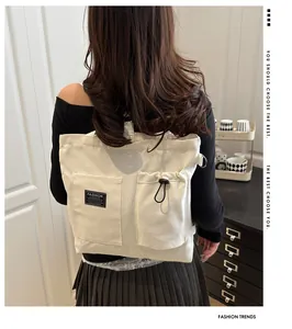 Detail view of large cargo pockets and adjustable drawstring on cream canvas shoulder bag