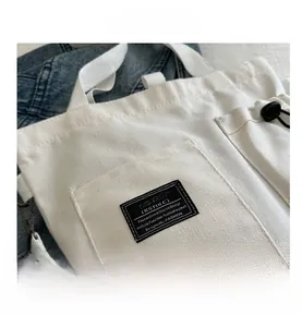 Detail of off-white canvas tote showing front pocket with fashion label and metal hooks