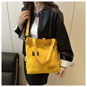 Detail of yellow canvas tote bag featuring large front pockets and black fashion label