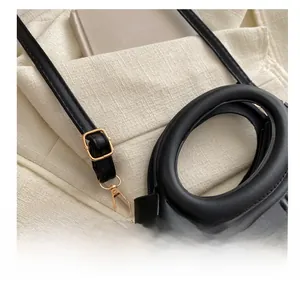 Detail of adjustable golden buckle and textured black faux leather strap of a handbag