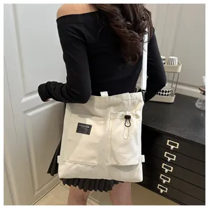 Detail of white canvas crossbody bag featuring front utility pockets and fashion label