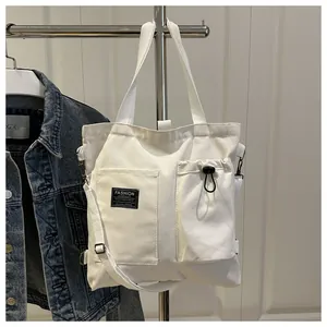 Close-up of white canvas tote bag featuring double front pockets and adjustable crossbody strap