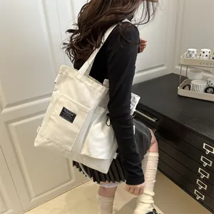 Minimalist white canvas tote bag with front pocket and shoulder strap in a stylish indoor setting