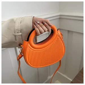 Detail of bright orange semi-circle handbag with vertical striped embossing and round handle