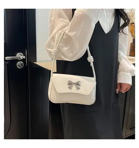 Dettaglio di una borsa sottobraccio bianca con fiocco argento e dettagli di corda annodata