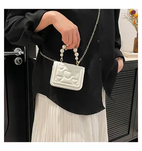 Close-up of white heart-quilted mini bag with elegant pearl handle and gold chain strap