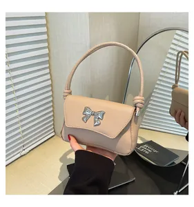 Dettaglio di borsa beige con fiocco metallico argento decorativo e manico con nodo