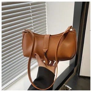 Detail of a brown leather crescent shoulder bag with metallic decorative buckle strap