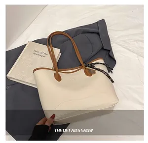 Detail of a large cream tote bag with brown handles and a woven pendant on white fabric