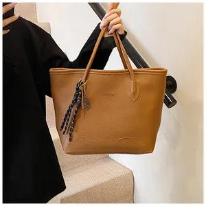 Detail view of caramel tote bag with litchi texture and metal tennis racket charm