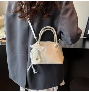 Detail der cremeweißen Ledertasche mit Spitzenschleife und Perlenanhänger