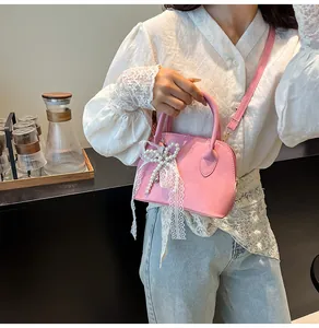 Detailaufnahme der rosa Muscheltasche mit weißer Spitzenschleife und Perlenanhänger