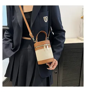 Model wearing a mini canvas and brown leather cylinder bucket bag with a gold zipper
