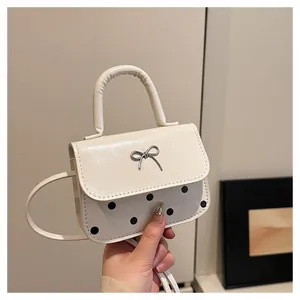 Detailansicht der cremefarbenen Handtasche mit schwarzen Punkten und Metallschleife
