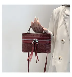Detail van bordeauxrode box tas met geweven textuur, zilveren ritsen en lange kwasten