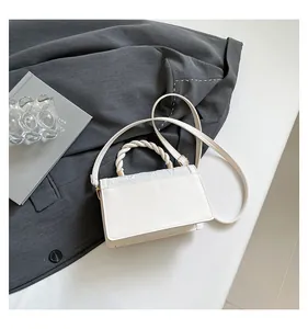 Detail of the woven twisted handle on a cream PU leather crossbody bag with a long strap