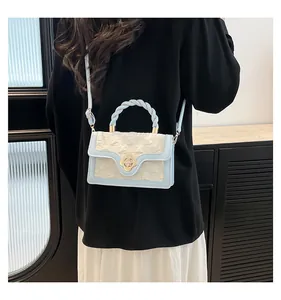 Detail of light blue crossbody bag with gold flower lock and woven handle held by model
