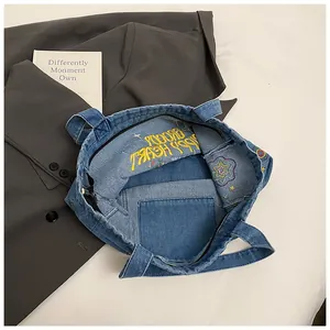 Detail view of denim tote bag featuring yellow embroidery and internal zipper pocket