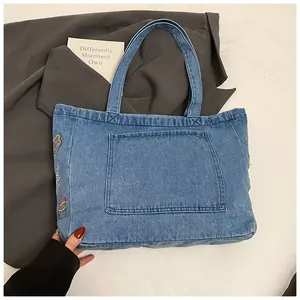 Close-up of blue denim tote bag featuring colorful embroidery and large front pocket