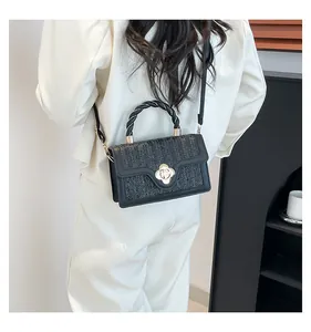 Detail of black crossbody bag with woven texture flap and gold petal clasp on model