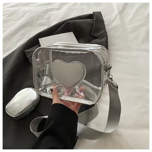 Detail of transparent PVC crossbody bag with silver heart patch and wide fabric strap