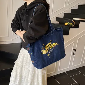 Large blue denim tote bag with colorful embroidery on a trendy commuter shoulder bag