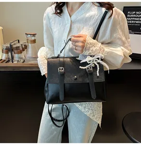 Dettaglio di una borsa messenger in pelle nera vintage con ciondolo di perle e lacci