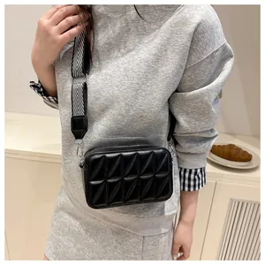 Detail van zwarte gewatteerde crossbodytas met zigzag canvas band gedragen door model