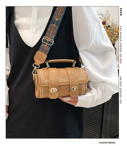 Close-up of a brown cylinder bag with bohemian wide strap and golden metal double locks