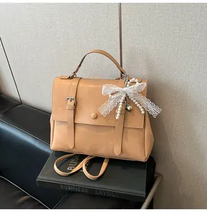 Dettaglio borsa vintage in pelle color cammello con fiocco in pizzo e perla su divano