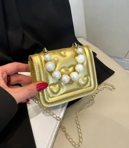 Detail van gouden mini-handtas met hartreliëf en handvat van witte parels voor dames