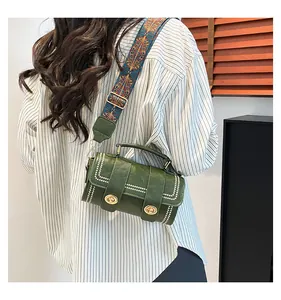 Detail of green cylinder bag featuring white rivet accents and ethnic woven wide strap