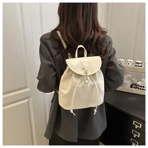 Détail d'un mini sac à dos en cuir crème avec cordon et crochet porté par un mannequin