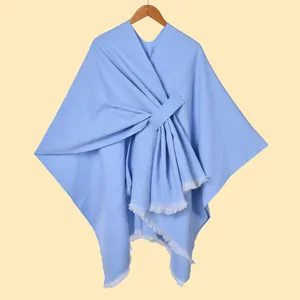 Detailed close-up of light blue knit poncho with fringe edges on wooden hanger