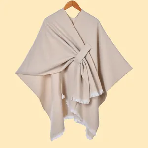 Detail of oat-colored knitted poncho showing crossbody tie and frayed fringe hemline
