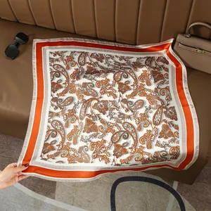 Détail d'un foulard en soie à motif paisley orange sur cuir avec des accessoires