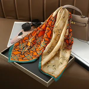 Silk-feel satin floral scarf with orange and green patterns draped on a handbag